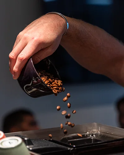 Hand som häller rostade kaffebönor ur en skål