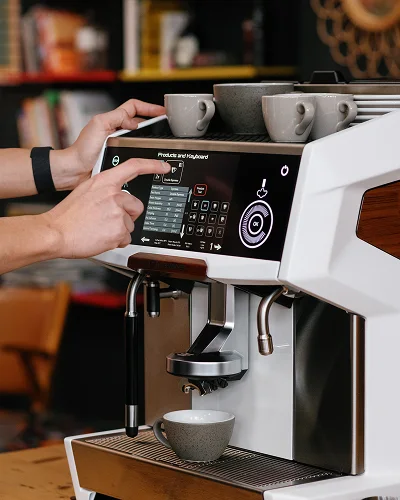 Händer som väljer dryck på pekskärmen på en Eversys kaffemaskin