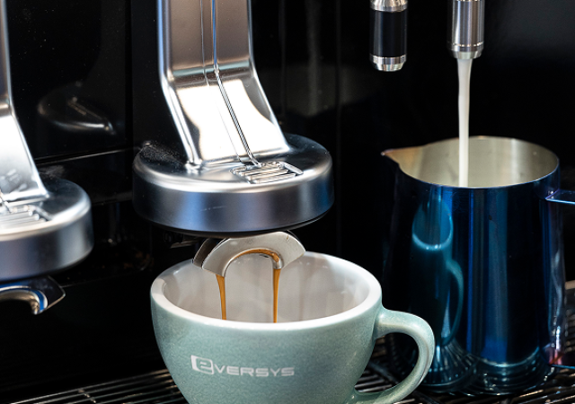 Mjölkkanna och kaffekopp under en Eversys espressomaskin